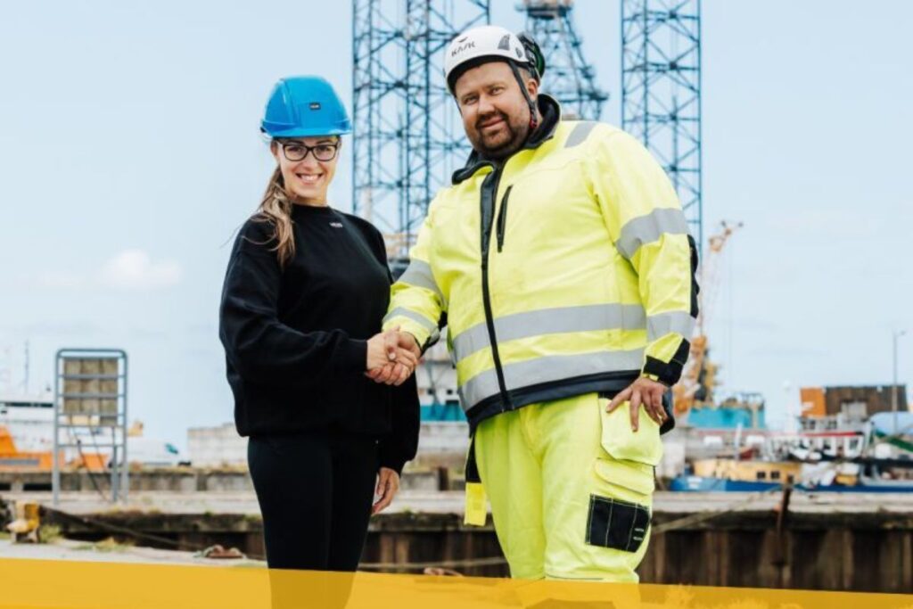 en rekrutteringspecialist og en industrimedarbejdere giver hånd på en havne- eller værftsarbejdsplads som symbol på aftale og mandskabsudlejning.