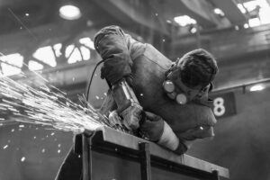 Smed sliber stålkonstruktion med vinkelsliber, mens gnister flyver i værkstedet.