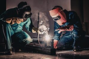 To svejsere i fuld beskyttelsesudstyr arbejder side om side med svejsearbejde i industrimilj
