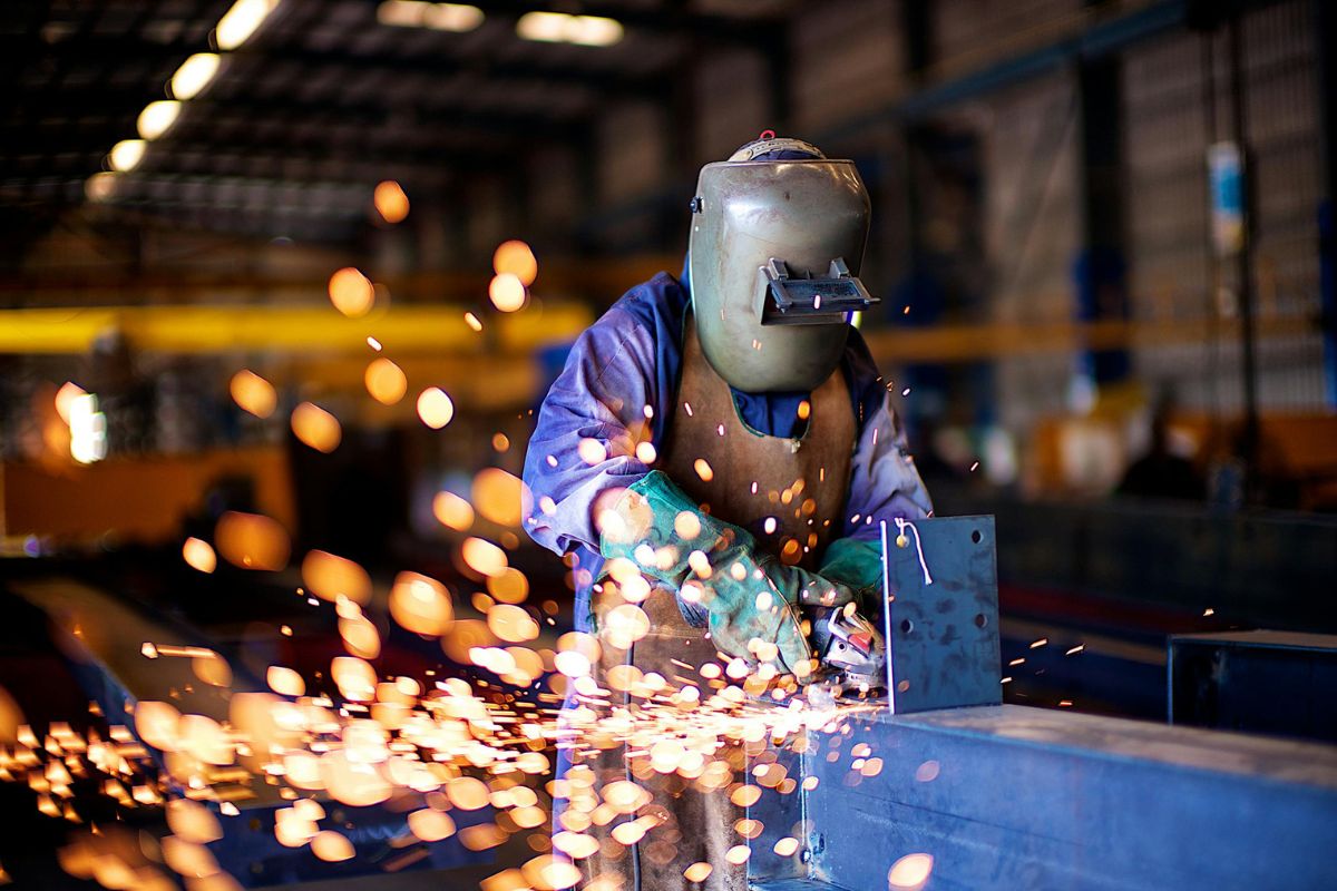 Svejser i fuld beskyttelsesudstyr arbejder med gnister i industriværksted under produktion